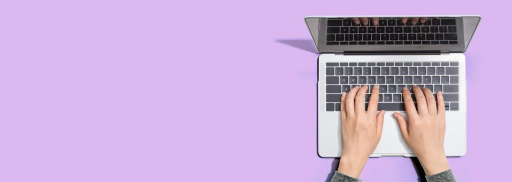 Mains tapant sur un ordinateur portable sur fond violet pastel