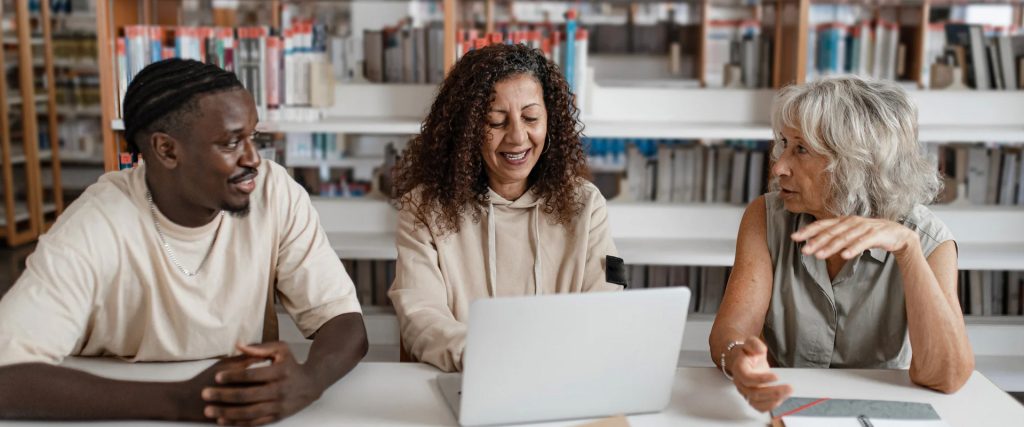 Groupe de personnes collaborant autour d'un ordinateur portable dans une bibliothèque